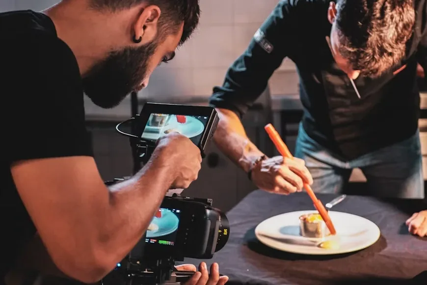 A videographer films a chef plating a dish in a restaurant kitchen