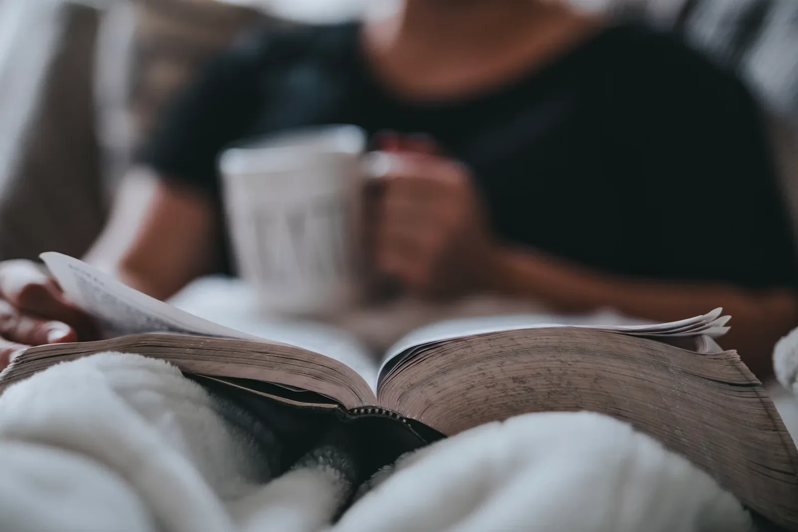 Someone relaxing on a sofa with a book and a mug of coffee